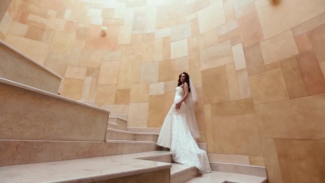 Full-length fottage of the attractive brunette with long curly hair and stylish dress posing on the yellow modern stairs.