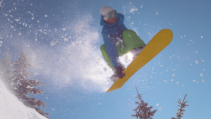 CLOSE UP: Spectacular shot of jumping snowboarder illuminated by winter sun.
