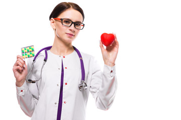 Young beautiful female doctor holding heart and pills in her hands on white background