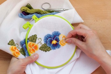Female hands are embroidering flowers on the canvas. Cross stitch technique.