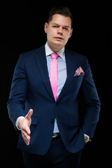 Portrait of confident handsome businessman offering his hand for handshake on black background