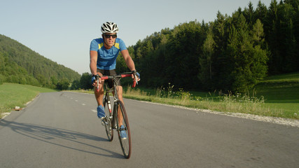 Naklejka premium Professional male cyclist cruises down empty asphalt road on a sunny spring day.