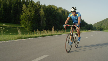 Obraz premium COPY SPACE: Pro biker man riding fast down asphalt road on his road bicycle.