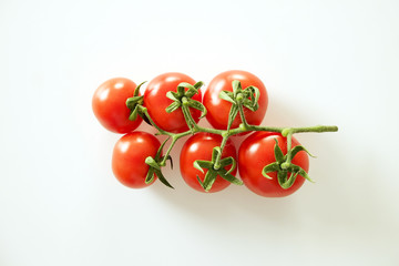 Branch of beautiful juicy organic red cherry tomatoes on white background. Top view of shiny polished glossy vegetables. Clean eating concept. Vegetarian vegan summer detox diet. Copy space, flat lay.