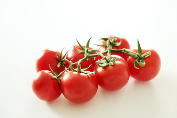 Branch of beautiful juicy organic red cherry tomatoes on white background. Top view of shiny polished glossy vegetables. Clean eating concept. Vegetarian vegan summer detox diet. Copy space, flat lay.