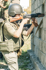 Fototapeta premium A young girl soldier shoots a rifle from behind a wall
