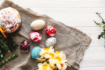 stylish painted eggs and easter cake on rustic wooden background with spring flowers and candle, top view. space for text. happy Easter concept, flat lay. seasons greetings