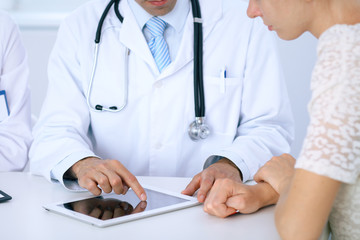 Doctor and  patient talking while sitting at the desk in office. Physician pointing into touch pad computer or tablet. Medicine and health care concept