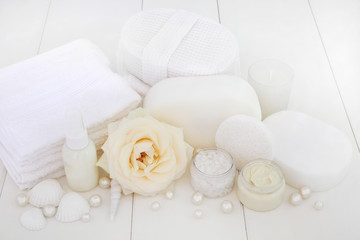 Spa beauty treatment products with a rose, ex foliating salt, moisturising cream, body lotion, sponges, wash cloths, shells and decorative pearls on white wood background.
