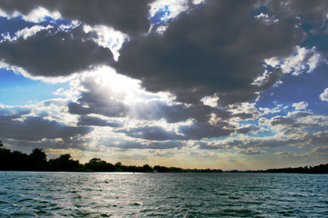 The rays of the sun make their way through the cumulus clouds in the blue sky and illuminate the navigable river.