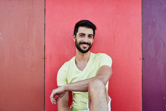 Handsome bearded man smiling at camera over colorful background.