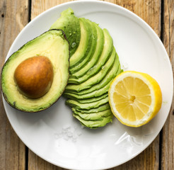 Avocado sliced on the white plate with lemon and half of avocado on the wooden rustic table