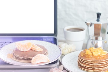 Workplace. Laptop with blank screen on table with breakfast: pancakes and coffee. Front view. Copy space
