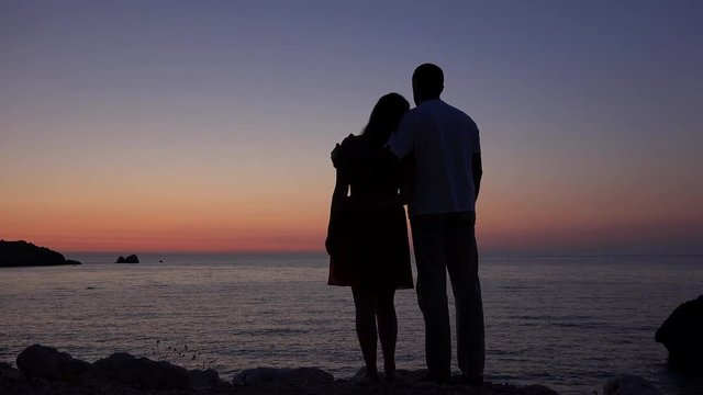 Couple of lovers silhouette standing embrace on seashore admiring sunset over sea
