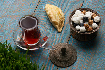Shekerbura with glass of tea and sweet snack on wooden table with wheat grass semeni, dessert for Novruz holiday