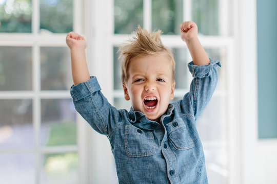 Cute young boy with wild hair screaming with his arms up
