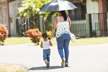 mother and son walking on street with umbrella on a sunny day