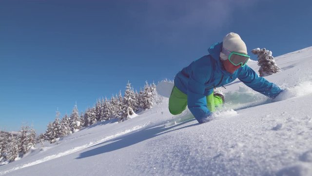SLOW MOTION, CLOSE UP: Pro male snowboarder on scenic ride down breathtaking mountains falls into fresh snow. Cool freeride guy falls while riding his snowboard on sunny day in the perfect backcountry