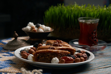 Plate with national pakhlava and snacks for Novruz with glass of tea on wooden table, close-up