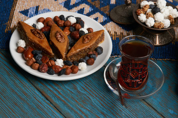 Plate with national pakhlava and snacks for Novruz with glass of tea on wooden table, close-up
