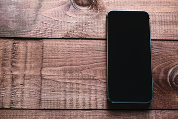 Top view of a modern smartphone with large screen on vintage wooden table. Blank empty display. Mock up