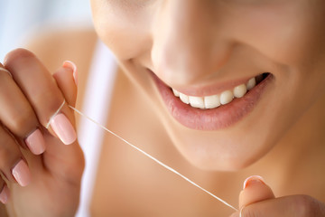 Close up of female face with perfect smile. Girl is cleaning teeth by special thread