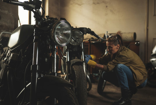 Young female working on restoration of old /vintage motorbikes in old rusty motorbike garage/workshop