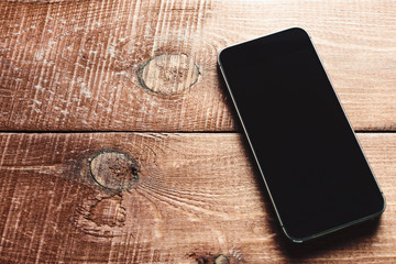 Top view of a modern smartphone with large screen on vintage wooden table. Blank empty display