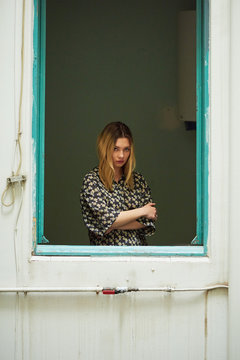 Sad blonde girl in shirt in unglazed window.