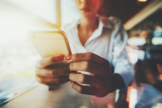 Closeup Wide-angle View Of The Hands With A Red Nails Of Afro Girl Sitting In In Cafe Indoors Next To A Window On A Sunny Day And Texting A Message To Her Family; Multiple Chromatic Aberrations Around