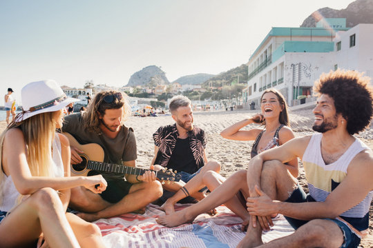 Young friends having fun and playing guitar at the beach