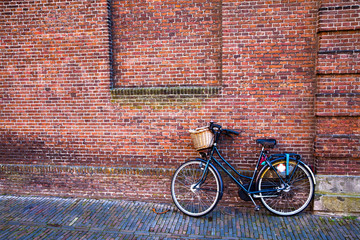 Bicycle with a basket standing on the street next to the brick wall on brick floor