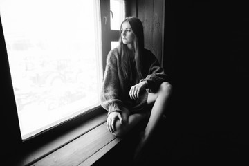 Silhouette portrait of depressed and sad young long-haired casual style woman sitting at the window in sweater, black and white tone, copy space, closeup