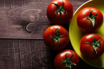 Freshly picked ripe tomatoes on a wooden retro table. Preparations for cooking. Vegetables lie on bright plates. Close up. Modern style