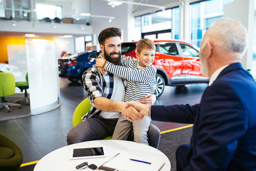 Father and son talking with a salesman about buying a new car at the car showroom.