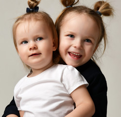 Beautiful little sisters sitting hugging each other happy smiling on gray 