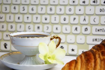 Stilllife of coffee cup with espresso, croissant or biscuit, flower and imitation of keyboard on a...