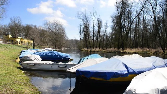 barche da fiume attraccate al molo coperte da teloni al primo sole dopo l'inverno