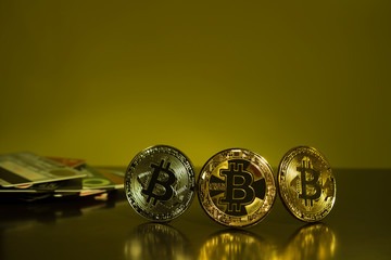 Bitcoin three coins closeup on reflective surface with dark yellow background