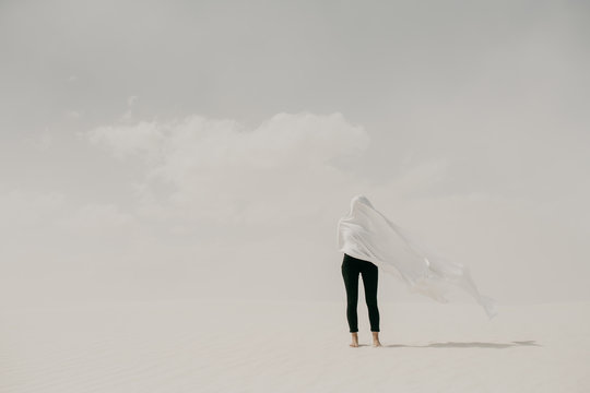 Contrast of woman wearing black with white fabric hiding her face in the minimal landscape