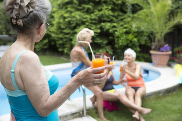 A woman with grey hair holding a glass of juice, looks at her fr