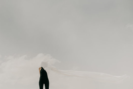 Contrast of woman wearing black with white fabric hiding her face in the minimal landscape
