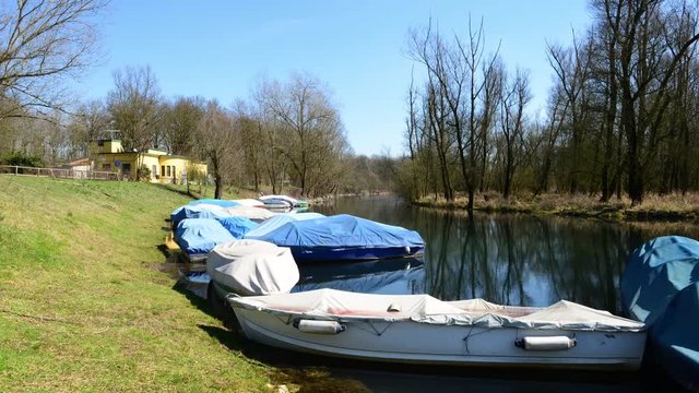 barche da fiume attraccate al molo coperte da teloni al primo sole dopo l'inverno