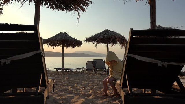 Kid on sunbed playing with feet in the sand, end of day on beach