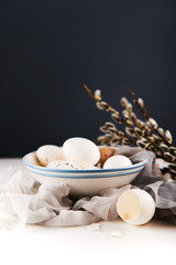Fototapeta na wymiar White eggs in bowl, broken egg shell, silk fabric and goat willow branches on a white table and dark background. Easter concept.