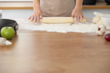 Female hands making dough for pizza or bread while using rolling pin. Baking concept