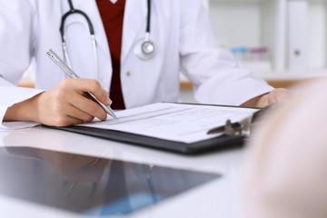 Close up of a female doctor filling up  an application form while consulting patient