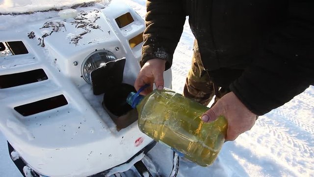 A man pours oil on a snowmobile