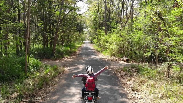 Slow motion Couple riding their scooter through forest.