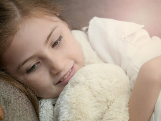 Cute caucasian blonde girl kid laying on sofa with doll feeling happy
